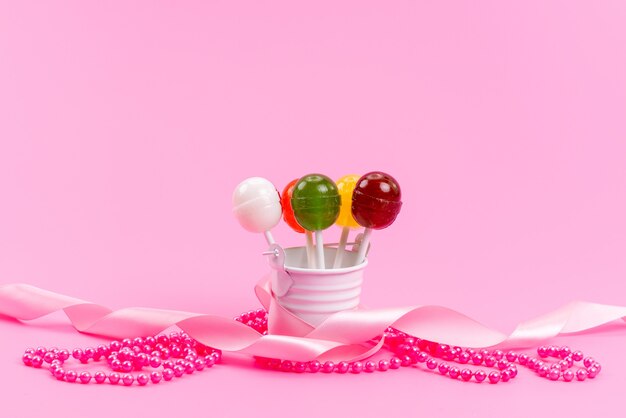 A front view colorful lollipops inside white, bucket on pink, sugar sweet confectionery candy