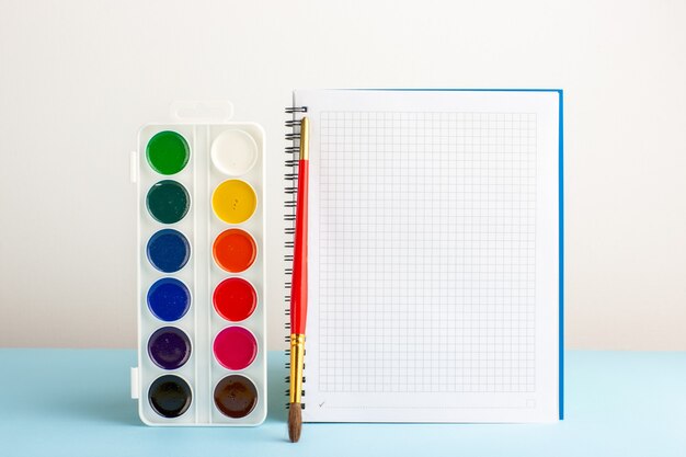 Front view colorful paints with copybook on blue desk