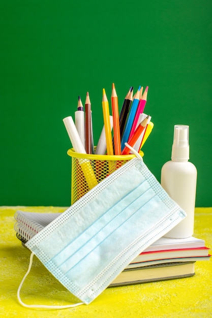 Вид спереди красочные карандаши с тетрадями и спреем на желтом столе