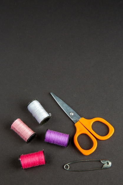 вид спереди разноцветные нитки с ножницами на темной поверхности темнота шитье одежды вязать женщина пришить булавку фото цвет