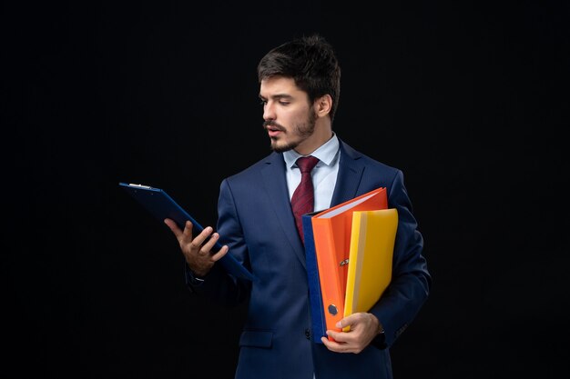 Free photo front view of concentrated young adult in suit holding several documents on isolated dark wall