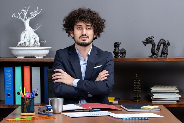 Free photo front view confident businessman crossing hands sitting at the desk in office