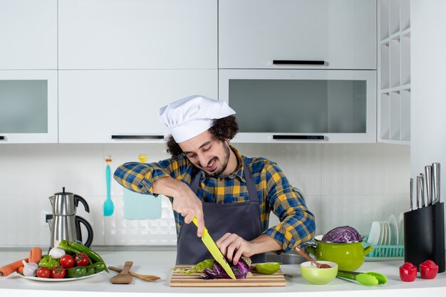 Front view of confident chef with fresh vegetables chopping foods in the white kitchen