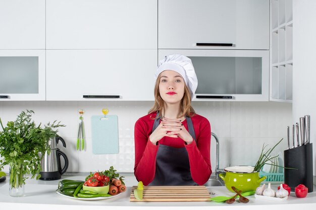 Front view confident female chef in uniform standing behind kitchen table