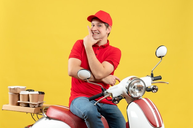 Вид спереди уверенно счастливого молодого парня в красной блузке и шляпе, доставляющего заказы на желтом фоне