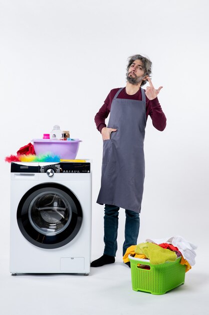 Front view confident housekeeper man putting hand in pocket standing near white washing machine on white background