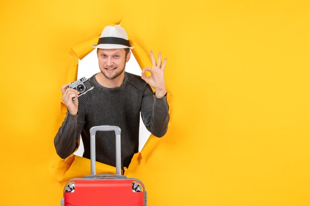 Front view of confident young adult holding bag and making eyeglasses gesture in a torn on yellow wall