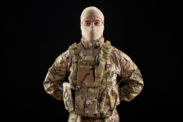 Вид спереди уверенного в себе молодого солдата в форме на черной стене