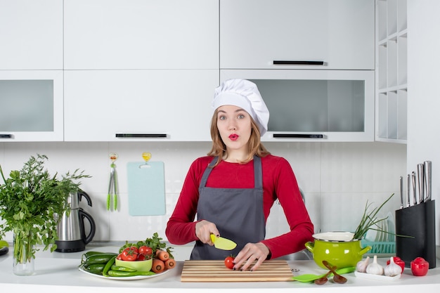 Front view confused female cook in apron cutting tomato