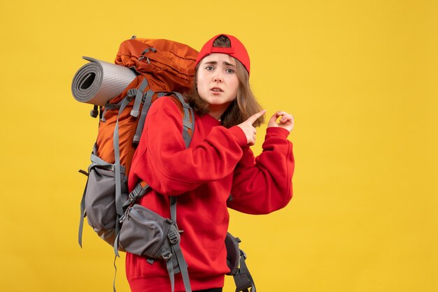 Front view confused female traveler with backpack pointing fingers behind