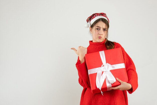 Front view confused girl with santa hat pointing at something