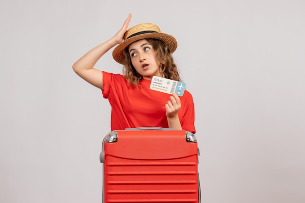 Front view of confused holiday girl with her valise holding ticket