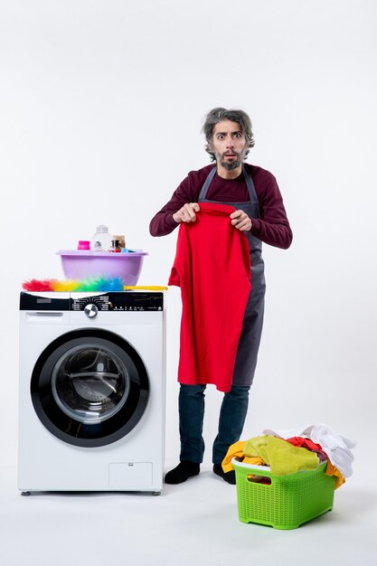 Front view confused housekeeper man holding towel standing near washing machine on white background