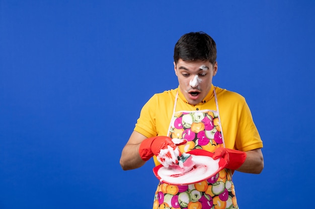 Front view confused housekeeper with foam on his face washing plate on blue space