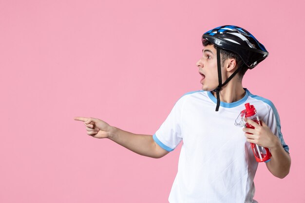 Front view confused male athlete in sport clothes with helmet and bottle of water