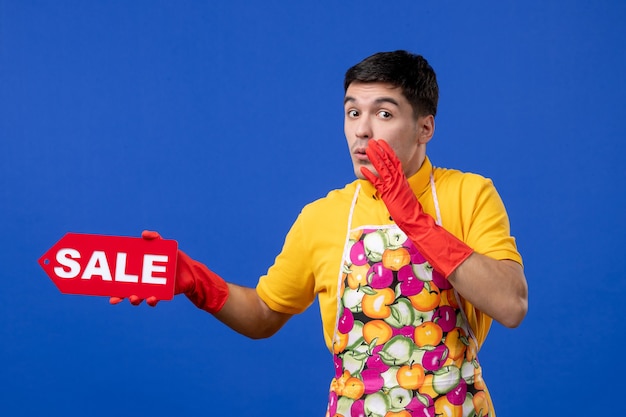 Front view confused male housekeeper in yellow t-shirt holding sale sign saying something on blue space