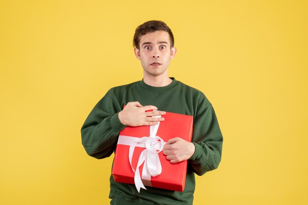 Front view confused man with green sweater holding gift on yellow 