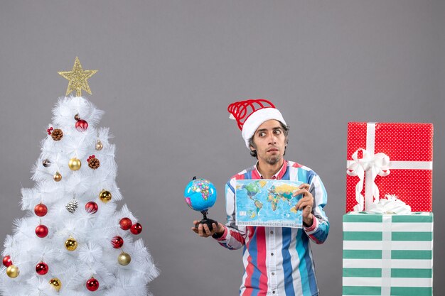 正面図は、クリスマスツリーとプレゼントの周りに世界地図と地球儀を保持しているスパイラルスプリングサンタ帽子と混乱した男