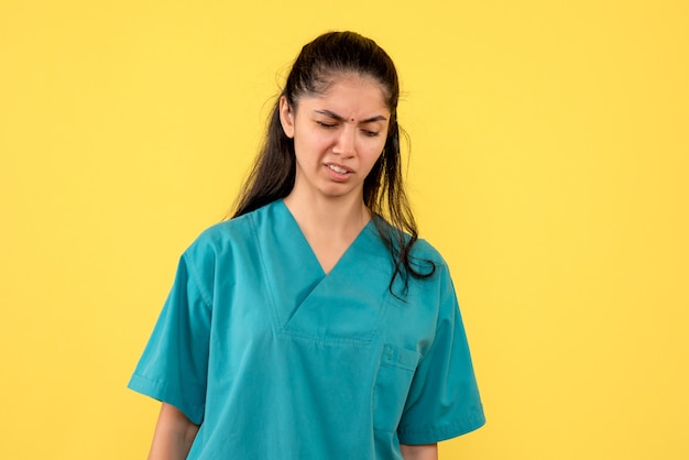 Front view confused pretty female doctor standing on yellow background