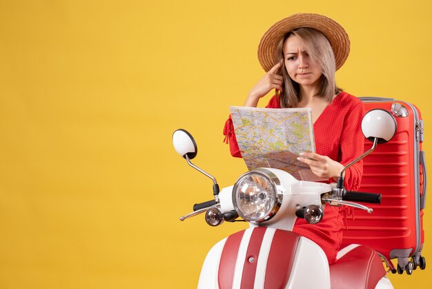 Front view of confused pretty girl on moped with big suitcase holding map