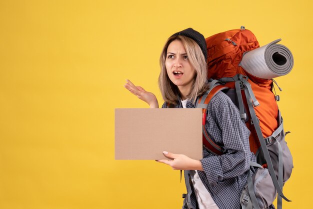 Front view of confused traveler woman with backpack holding cardboard