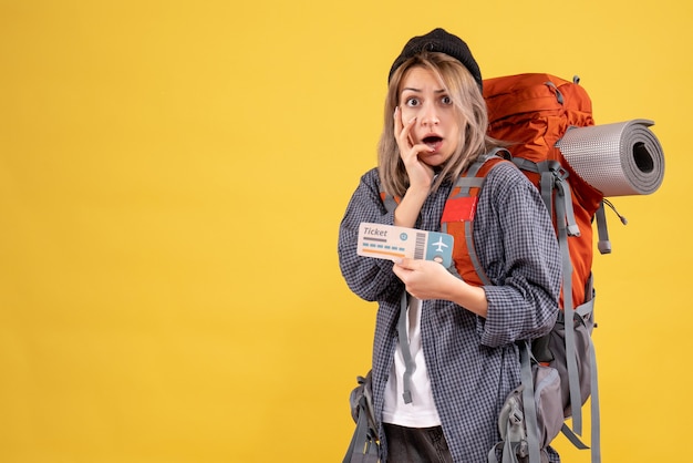 Front view of confused traveler woman with backpack holding ticket