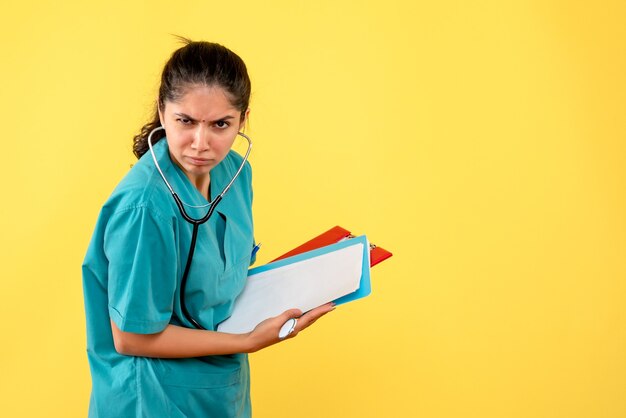 Front view confused woman doctor in uniform standing with papers on yellow background