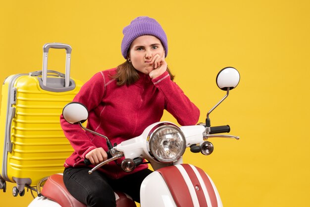 Front view confused young girl on moped with yelow suitcase