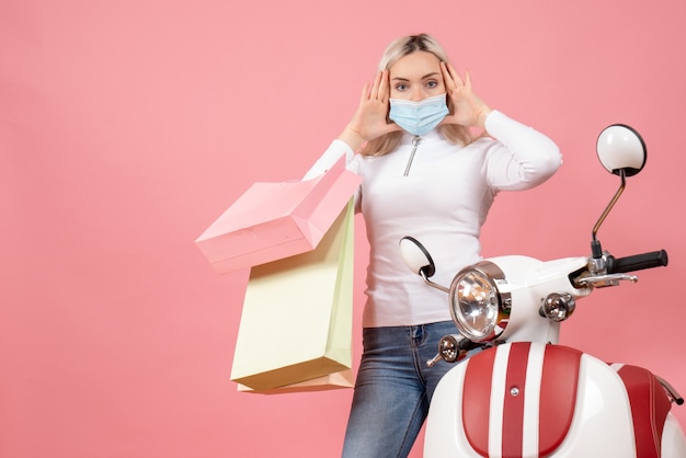 Front view confused young lady holding shopping bags near moped