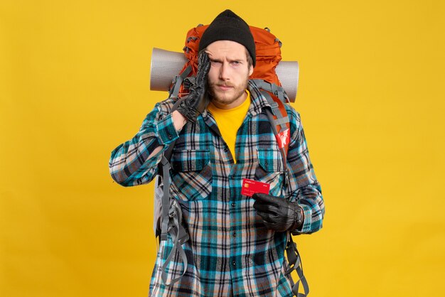 Front view of confused young male with backpacker holding bank card