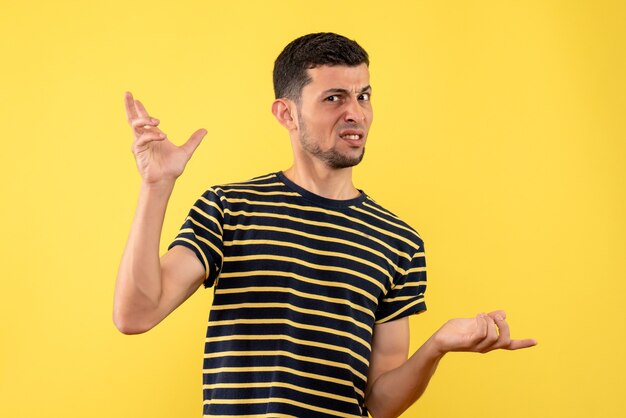 Front view confused young man in black and white striped t-shirt opening hands on yellow isolated background