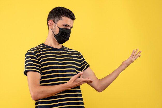 Front view confused young man in black and white striped t-shirt yellow background