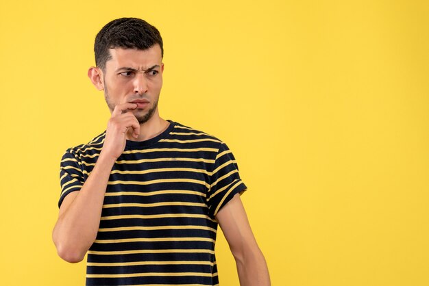 Front view confused young man in black and white striped t-shirt yellow isolated background copy place