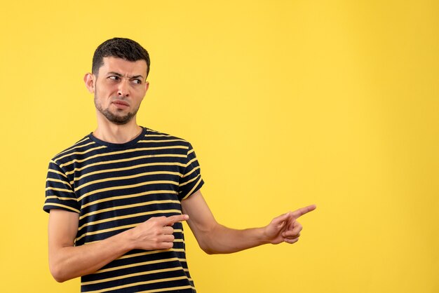 Front view confused young man in black and white striped t-shirt on yellow isolated background