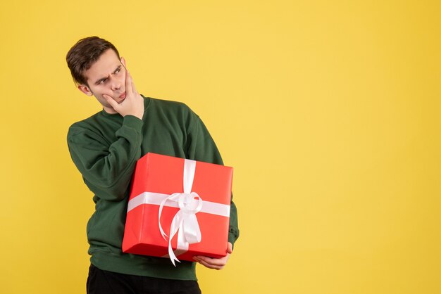 Front view confused young man with green sweater standing on yellow 