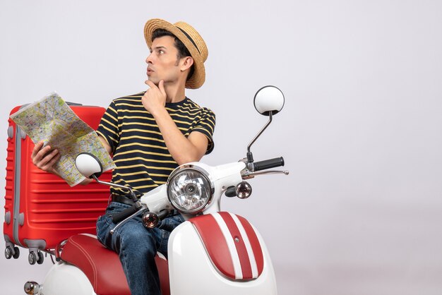 Front view of confused young man with straw hat on moped holding map looking something