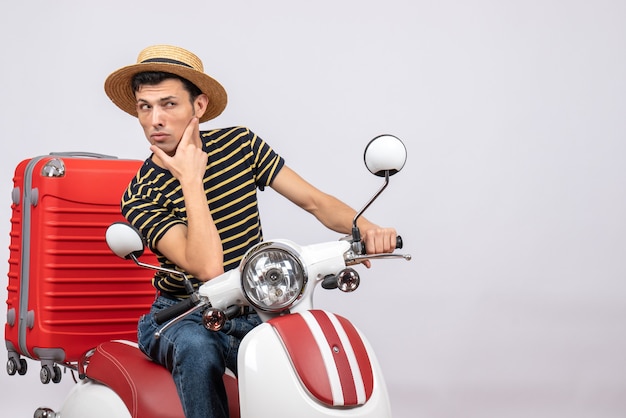 Front view confused young man with straw hat on moped looking at something