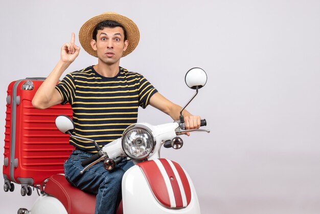 Front view of confused young man with straw hat on moped pointing at ceiling