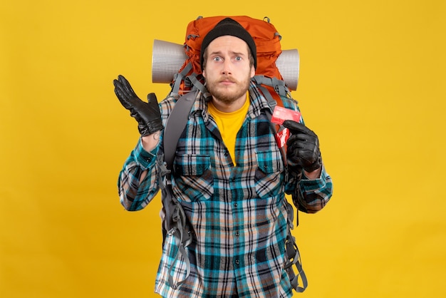 Front view of confused young traveler with backpacker holding credit card