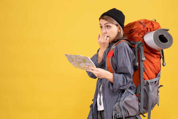 Front view of confused young traveller with backpack holding map standing on yellow wall