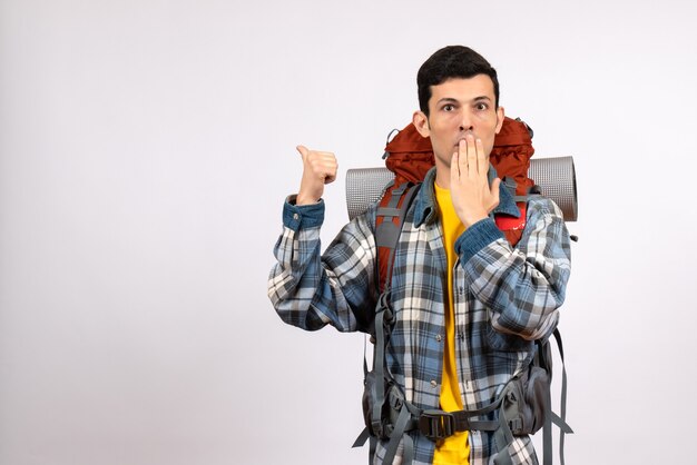 Front view confused young traveller with backpack pointing at behind