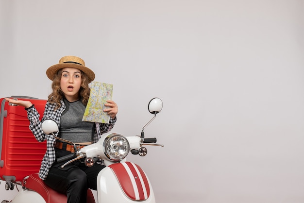 Front view of confused young woman on moped holding map on grey wall