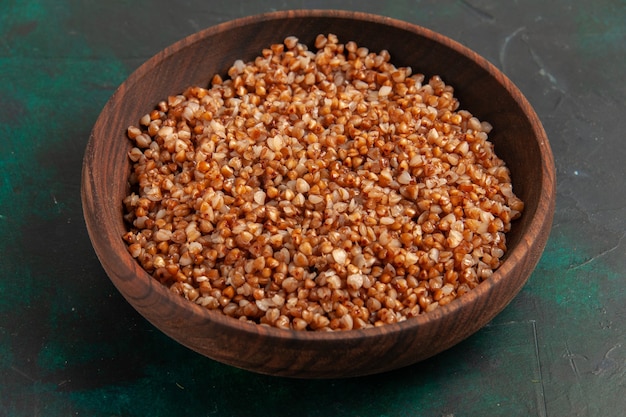 Front view cooked buckwheat tasty meal inside brown plate on the dark green surface