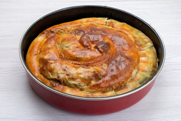 Front view of cooked greens cake inside round pan on the white surface