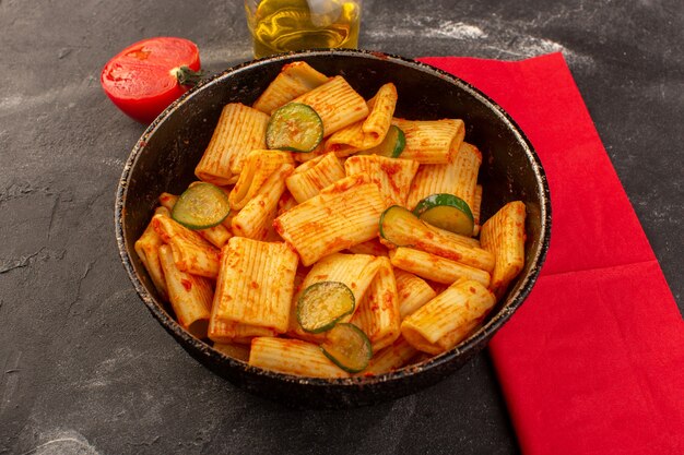 A front view cooked italian pasta with tomato sauce and cucumber inside pan on the dark desk