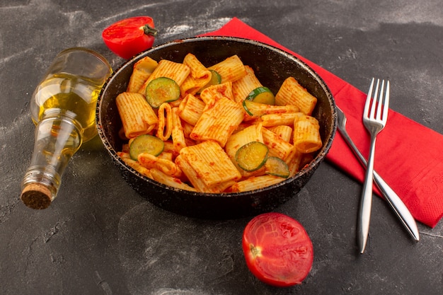 A front view cooked italian pasta with tomato sauce and cucumber inside pan on the dark desk