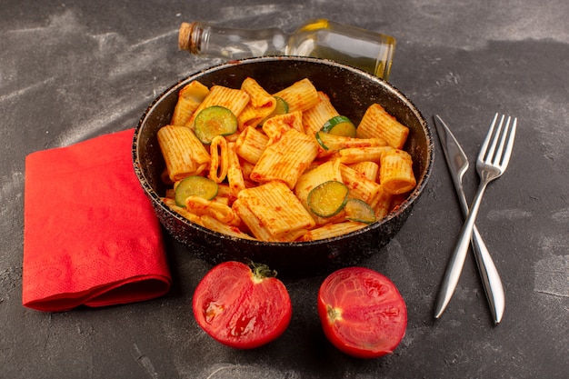 Вид спереди приготовленные итальянские макароны с томатным соусом и огурцом внутри сковороды на темной поверхности