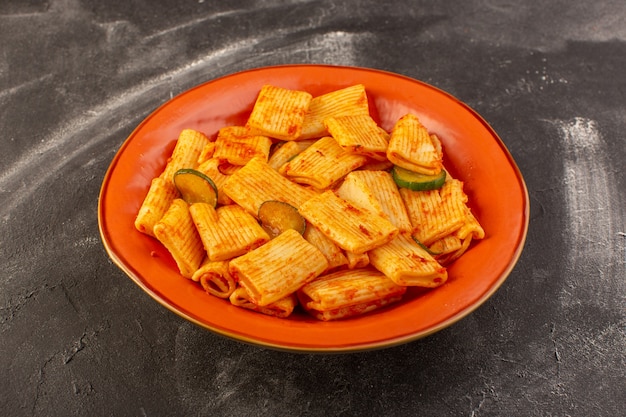 Вид спереди приготовленные итальянские макароны с томатным соусом и огурцом внутри тарелки на темной поверхности