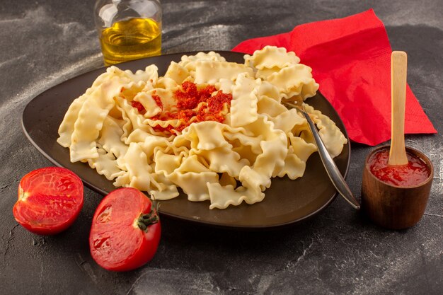 Вид спереди приготовленные итальянские макароны с томатным соусом внутри тарелки на серой поверхности