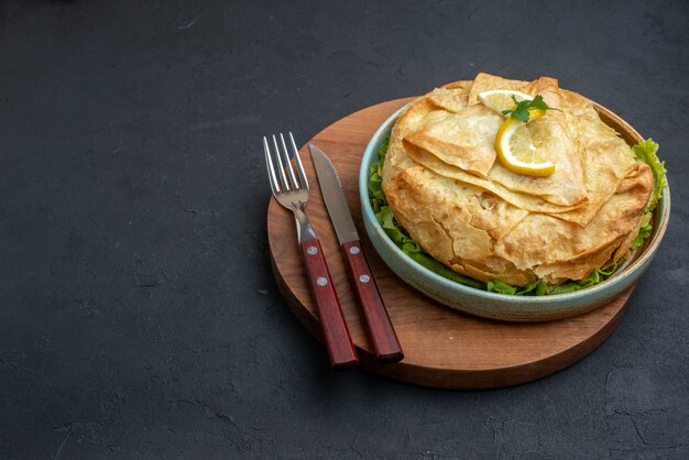 Front view cooked pita inside plate with greens and lemon slices on dark surface